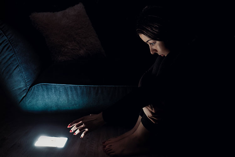 Ragazza seduta per terra nel buio che fissa lo schermo mentre guarda porno