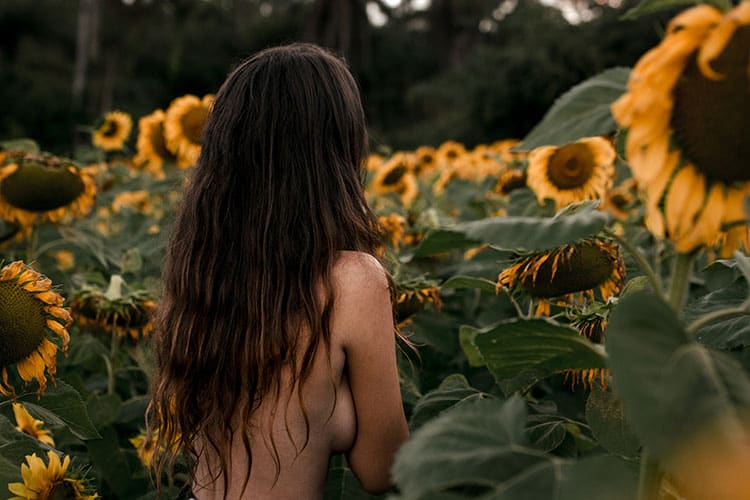 donna con il seno nudo in mezzo a un campo di girasoli