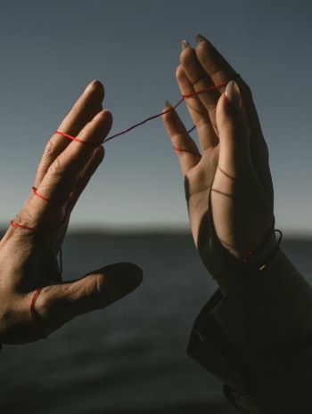 Illustration photographique de deux mains reliée par par un fil rouge